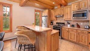Una cocina con armarios de madera, una isla central con taburetes de bar, un refrigerador de acero inoxidable, una estufa y un microondas.