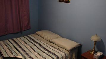 A bedroom with a bed, a bedside lamp, a nightstand, a picture on the wall, and a window with curtains.