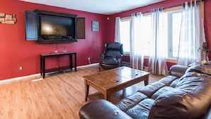 A living room with a red wall, a wooden coffee table, a leather sofa, a television, and a window with curtains. - Wild North Bed & Rest (Whitehorse)