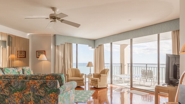 A spacious living room with a large sofa, a television, and a balcony with a view of the ocean. - Surfmaster - Oceanfront 3 Bedroom/3 Bath  Beautiful!!! Great Rates!! (Garden City)