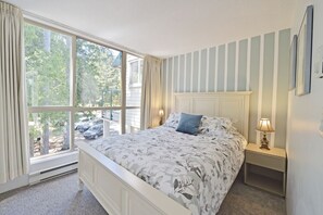 A bedroom with a large window, a bed with floral bedding, a nightstand with a lamp, and a striped wall.