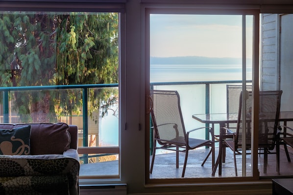 A room with a sliding glass door leading to an outdoor patio with a view of a lake and mountains.