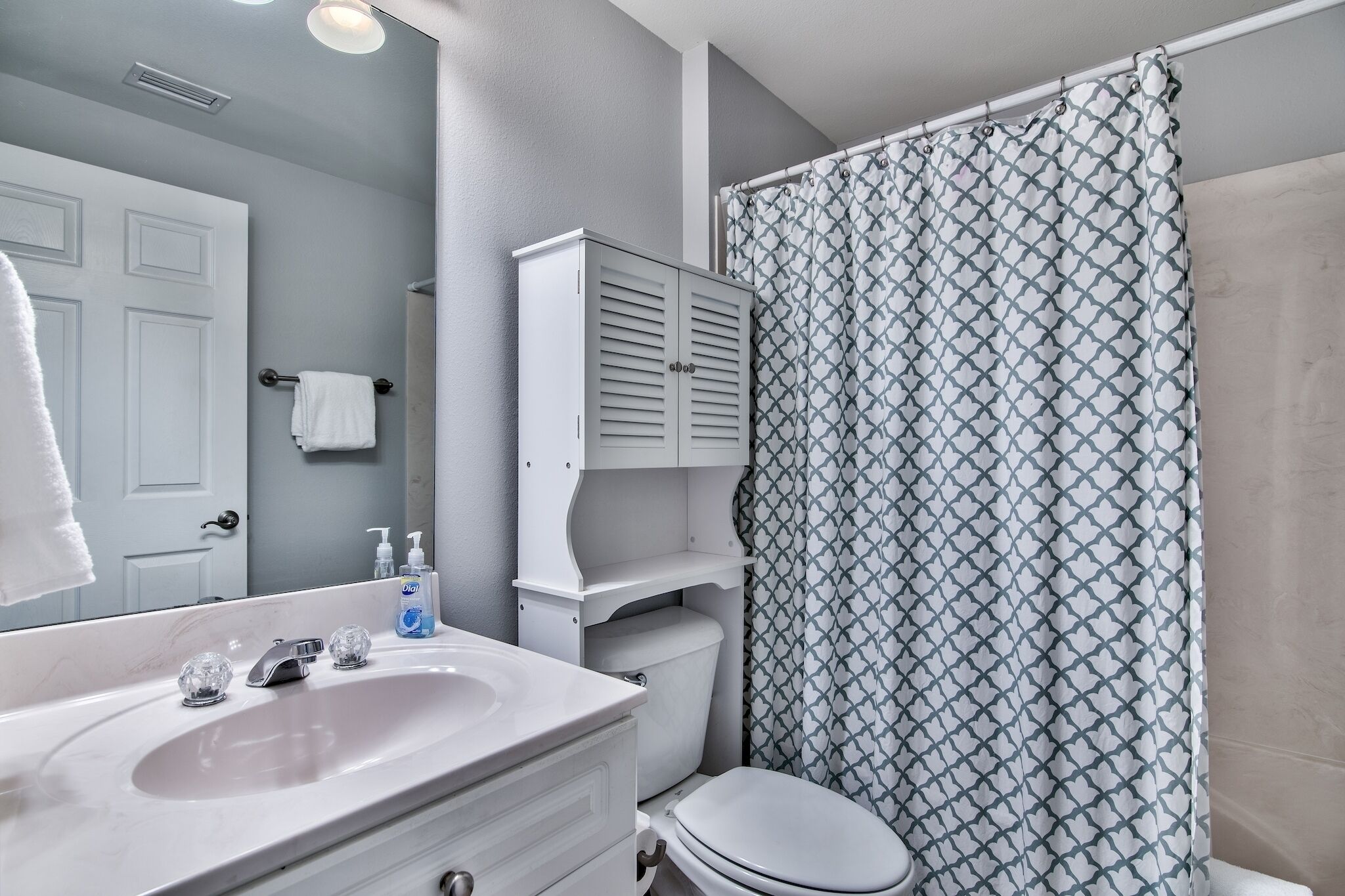 A bathroom with a white sink, mirror, and toilet. There is a shower curtain with a geometric pattern.