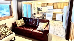 A living room with a leather sofa, a dining table, and a kitchen area with wooden cabinets and white appliances. - 2 Bedroom 2 Bathroom Condo - Base Area - Three Seasons (Mount Crested Butte)