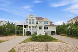 A two-story house with a covered porch, a staircase leading to the second floor, and a basketball hoop in the yard.