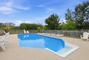 A swimming pool with lounge chairs and a wooden fence.