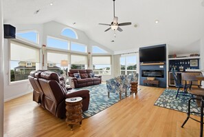 A spacious living room with a large window, a ceiling fan, a fireplace, and a TV.
