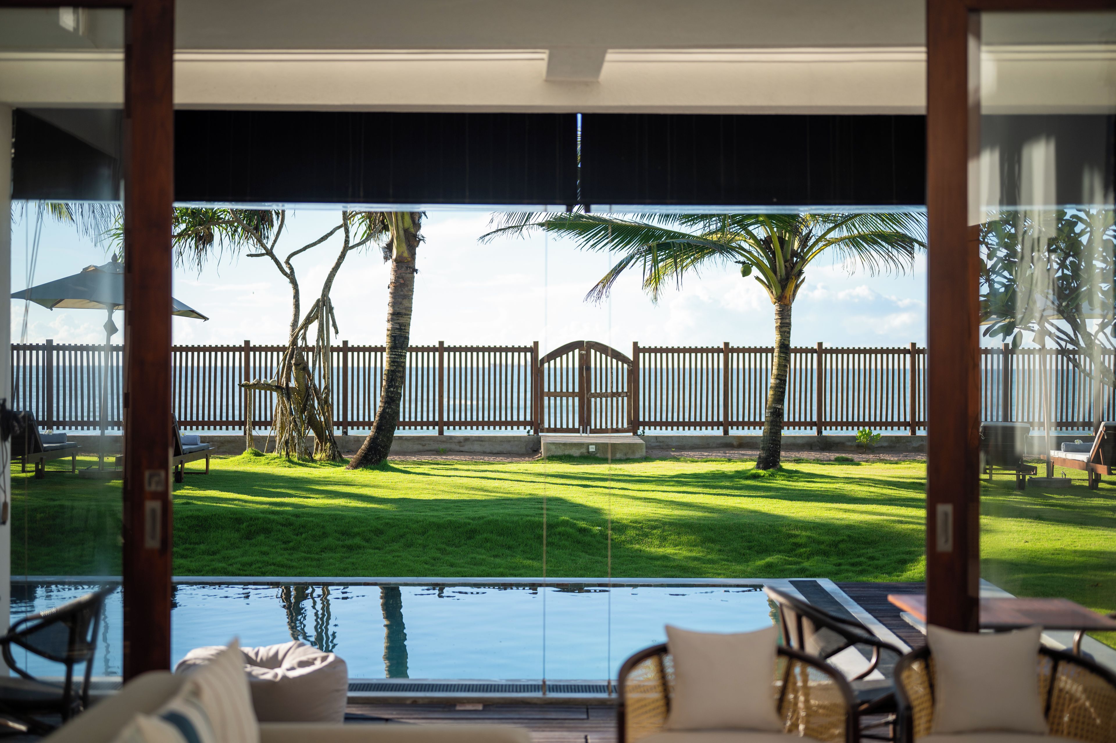 A poolside area with a view of a fenced yard, palm trees, and a wooden deck.