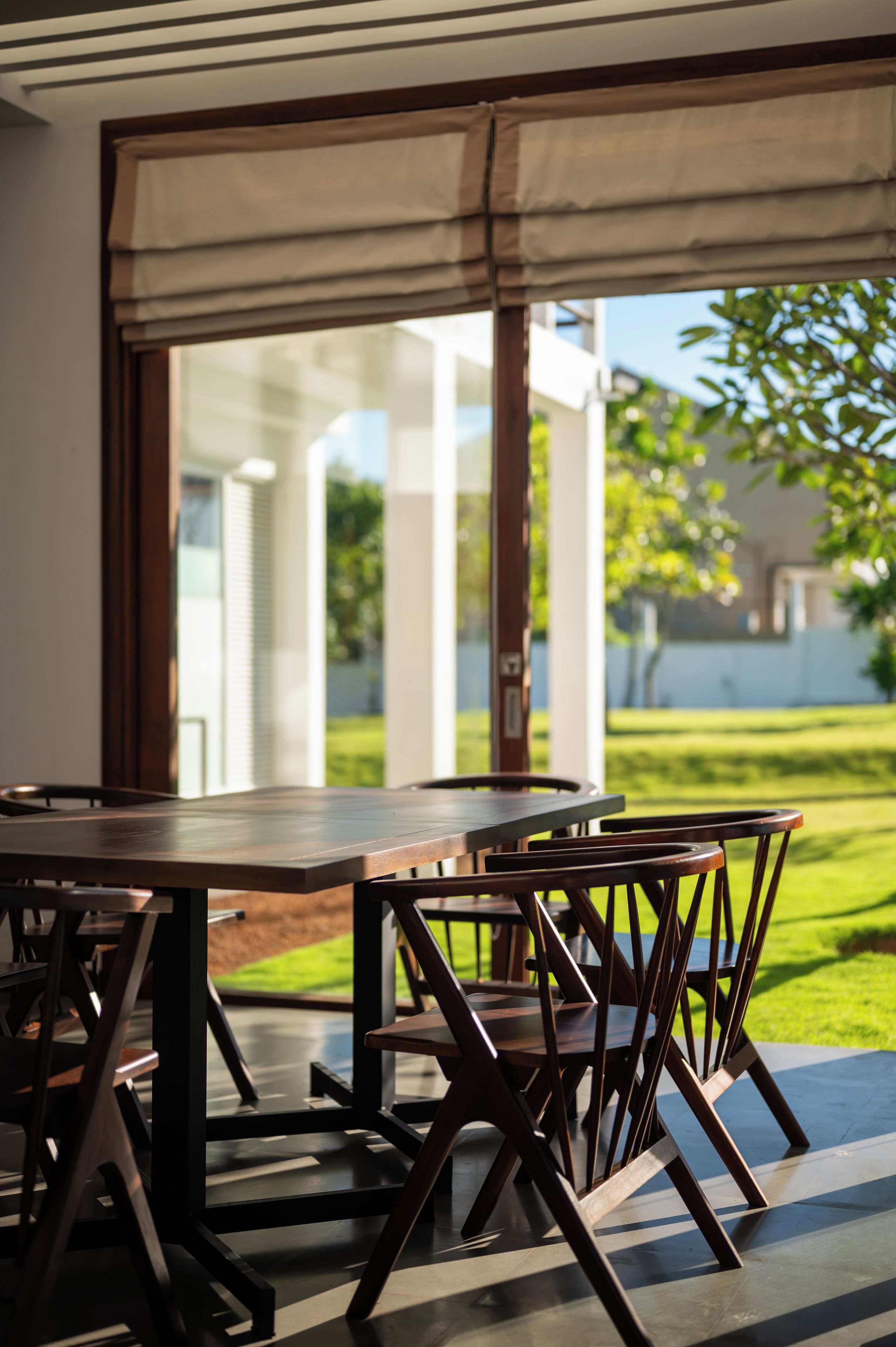 Un área de comedor al aire libre con una mesa y sillas, vista a un jardín y un edificio al fondo.