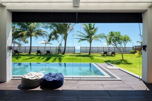 A pool area with a view of the sea, palm trees, and a wooden deck with bean bags. - Céu Ceylon (Kalametiya)