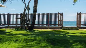 A poolside view with a wooden fence, palm trees, and a clear view of the ocean.