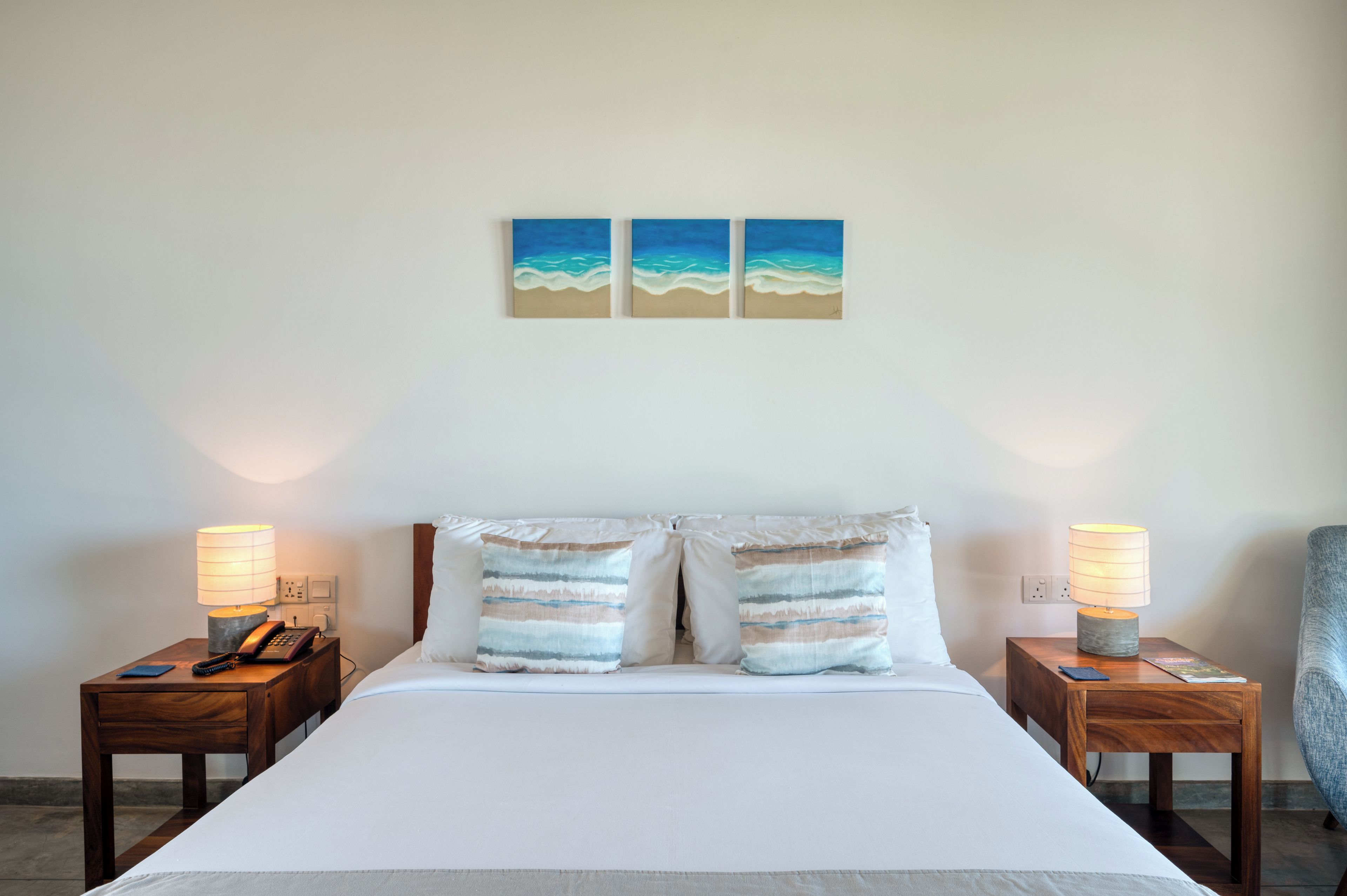 A hotel room with a bed, two bedside tables, lamps, and two wall-mounted paintings.
