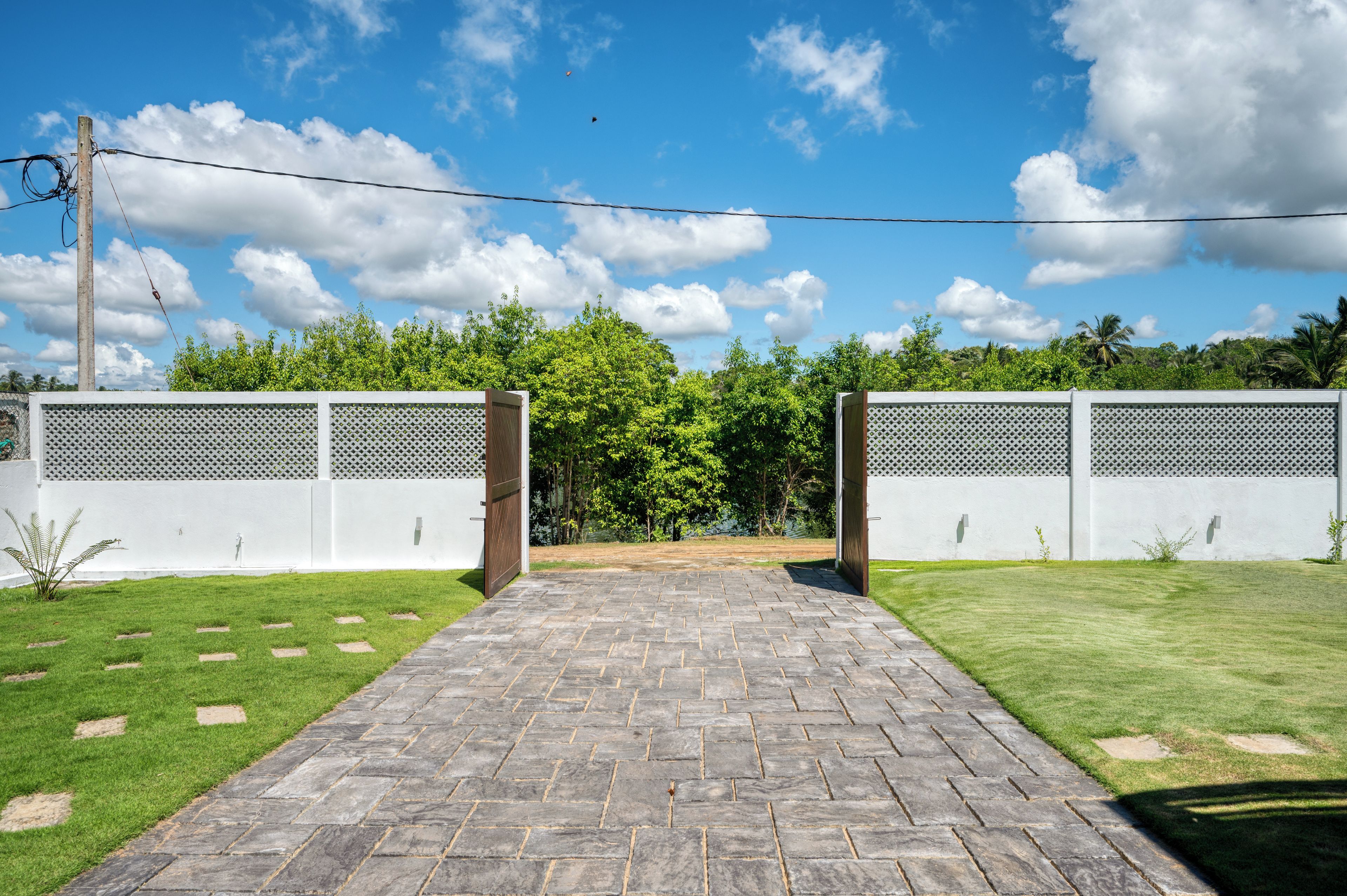Entrada pavimentada para uma propriedade com cerca branca e céu claro.