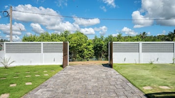 Entrada pavimentada para uma propriedade com cerca branca e céu claro.