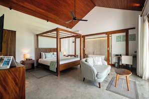 A modern bedroom with a four-poster bed, a sitting area with a sofa and armchair, and a small wooden table. - Céu Ceylon (Kalametiya)