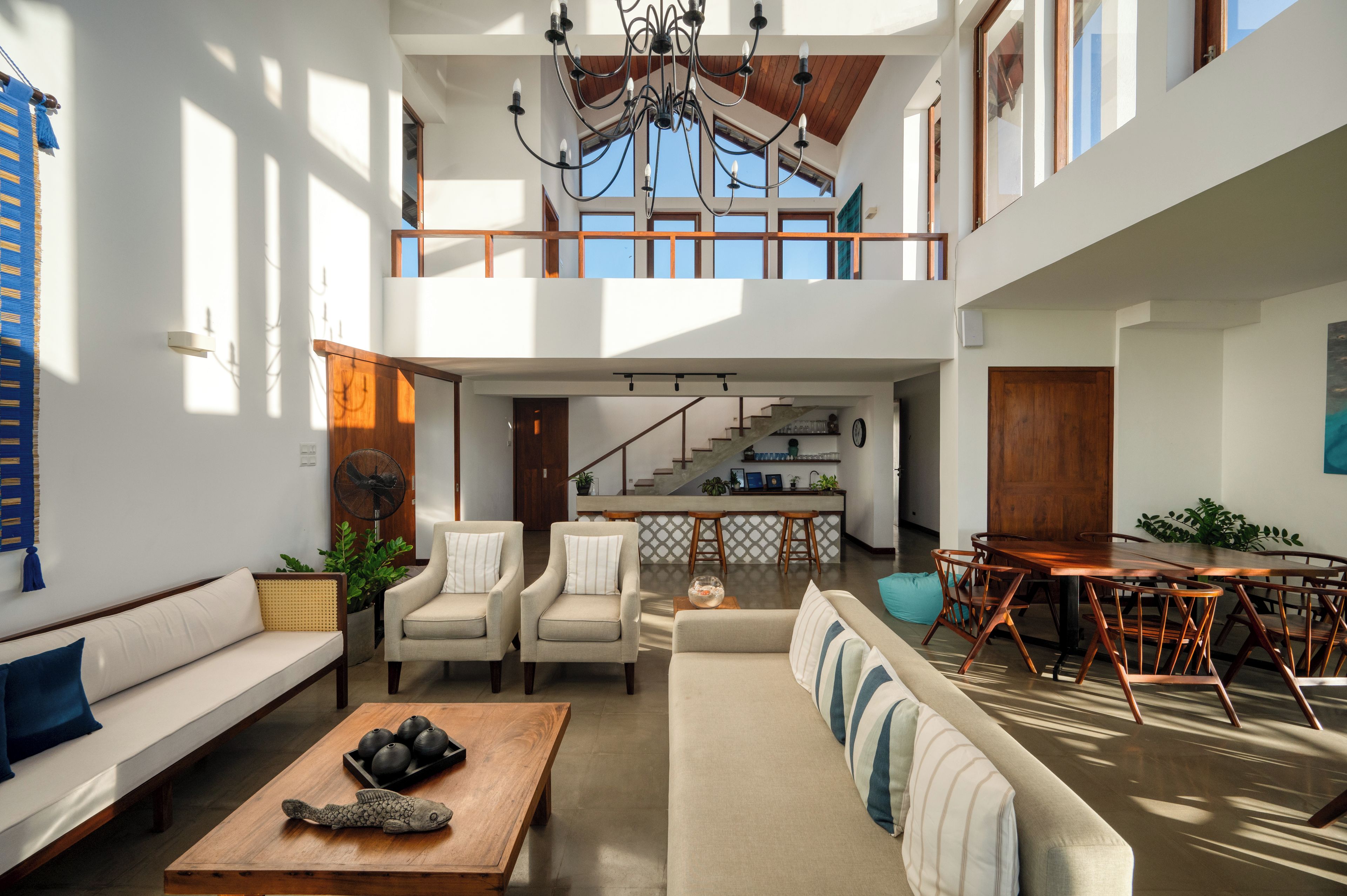 A spacious living area with a high ceiling, a staircase leading to an upper level, and a dining area with wooden furniture.