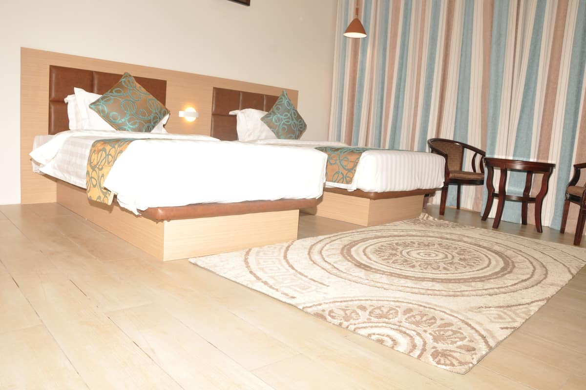 A hotel room with two beds, a wooden headboard, a striped curtain, and a wooden chair.