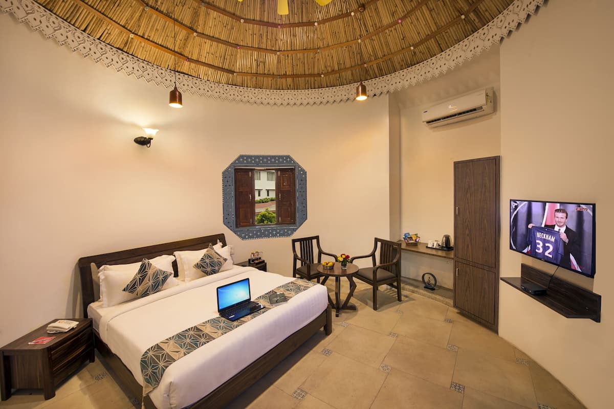 A hotel room with a bed, a laptop, a TV, a dining table, and chairs.