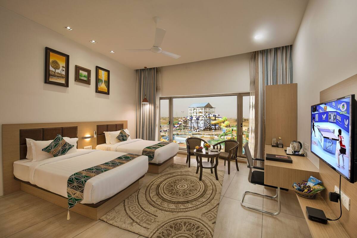 A hotel room with a bed, two bedside tables, a desk with a TV, a chair, and a view of an outdoor pool area.