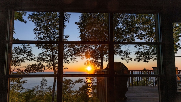 Une vue sur le coucher de soleil à travers une fenêtre, avec une terrasse en bois et une rambarde.