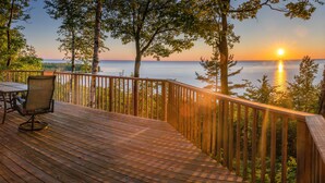 Une terrasse en bois, agréée de mobilier d’extérieur, qui offre une vue sur une étendue d’eau au coucher du soleil.