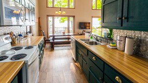 Une cuisine moderne avec des plans de travail en bois, une cuisinière encastrée et un coin repas offrant une vue sur l’extérieur.