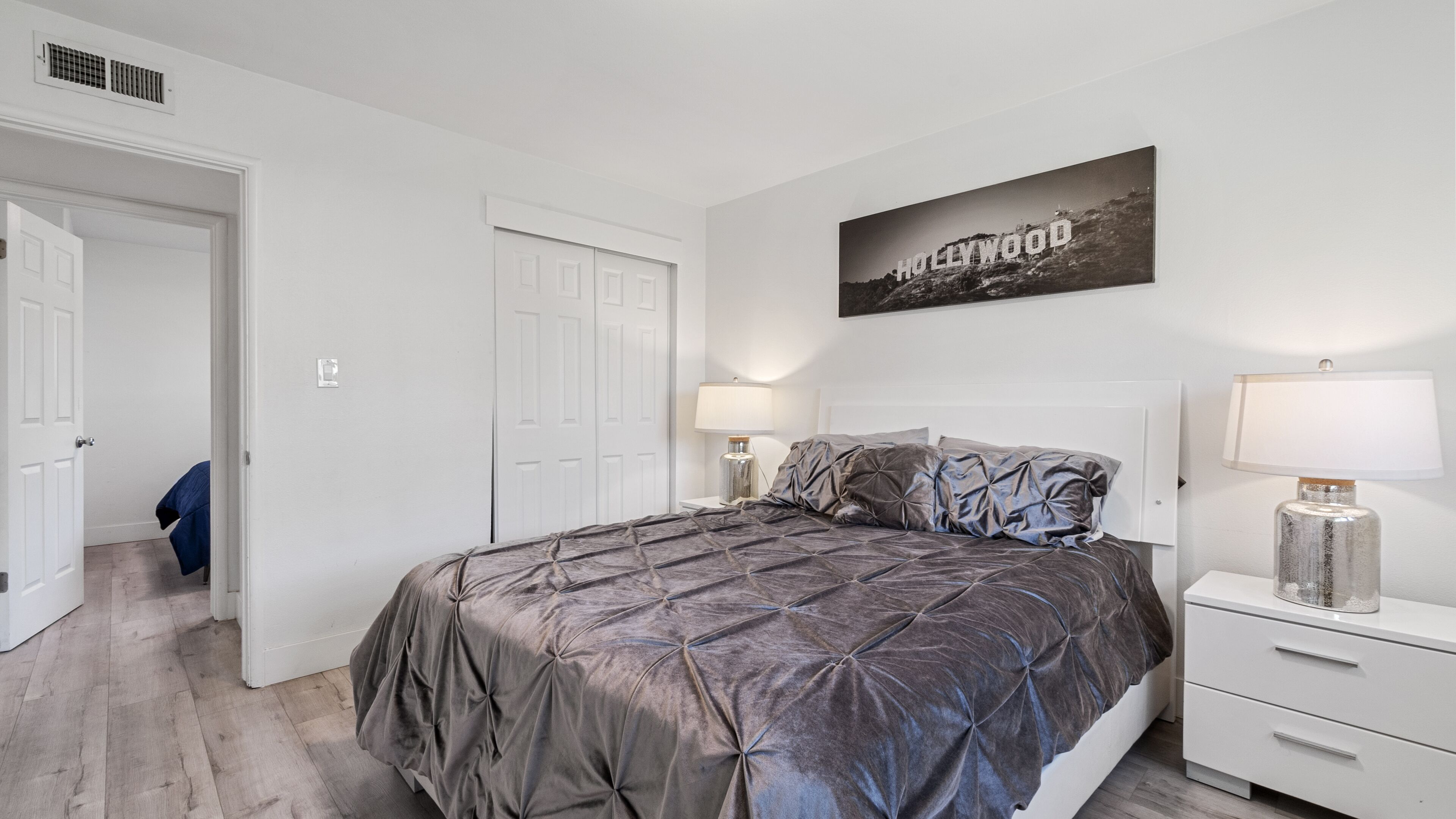 Un dormitorio con una cama, dos mesitas de noche, una lámpara de pared, una puerta y una fotografía del cartel de Hollywood.