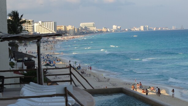 Una playa con zona de piscina, sillas de descanso y vistas al océano y al horizonte de la ciudad.