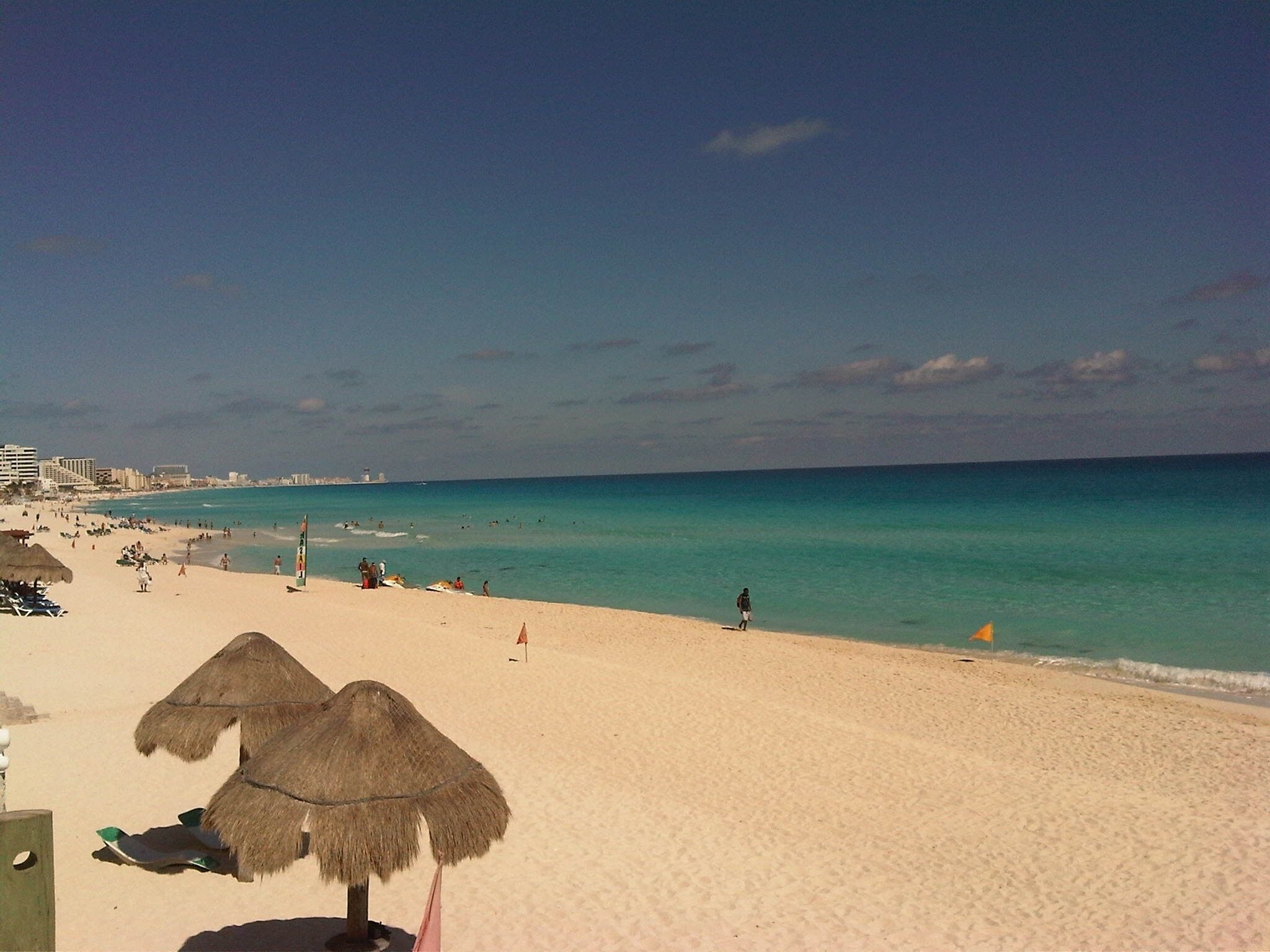 A beach with thatched umbrellas, a sandy shore, and a clear blue sea.