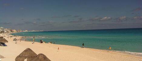 A beach with thatched umbrellas, a sandy shore, and a clear blue sea.