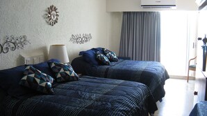 Habitación de hotel con dos camas, un reloj de pared y un ventanal con cortinas.