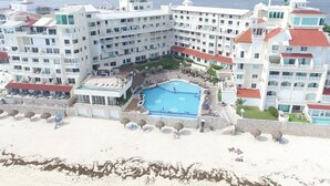 Un hotel grande con varios pisos, una piscina central y una zona de playa.