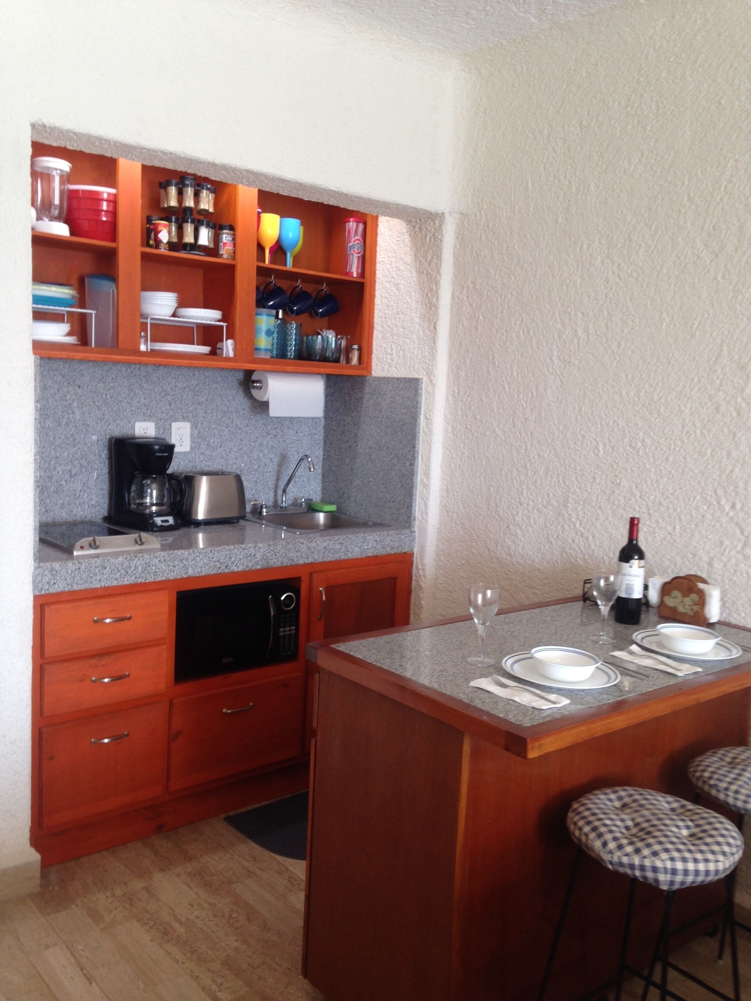 A compact kitchen with a built-in coffee maker, a sink, and a small dining area with stools.