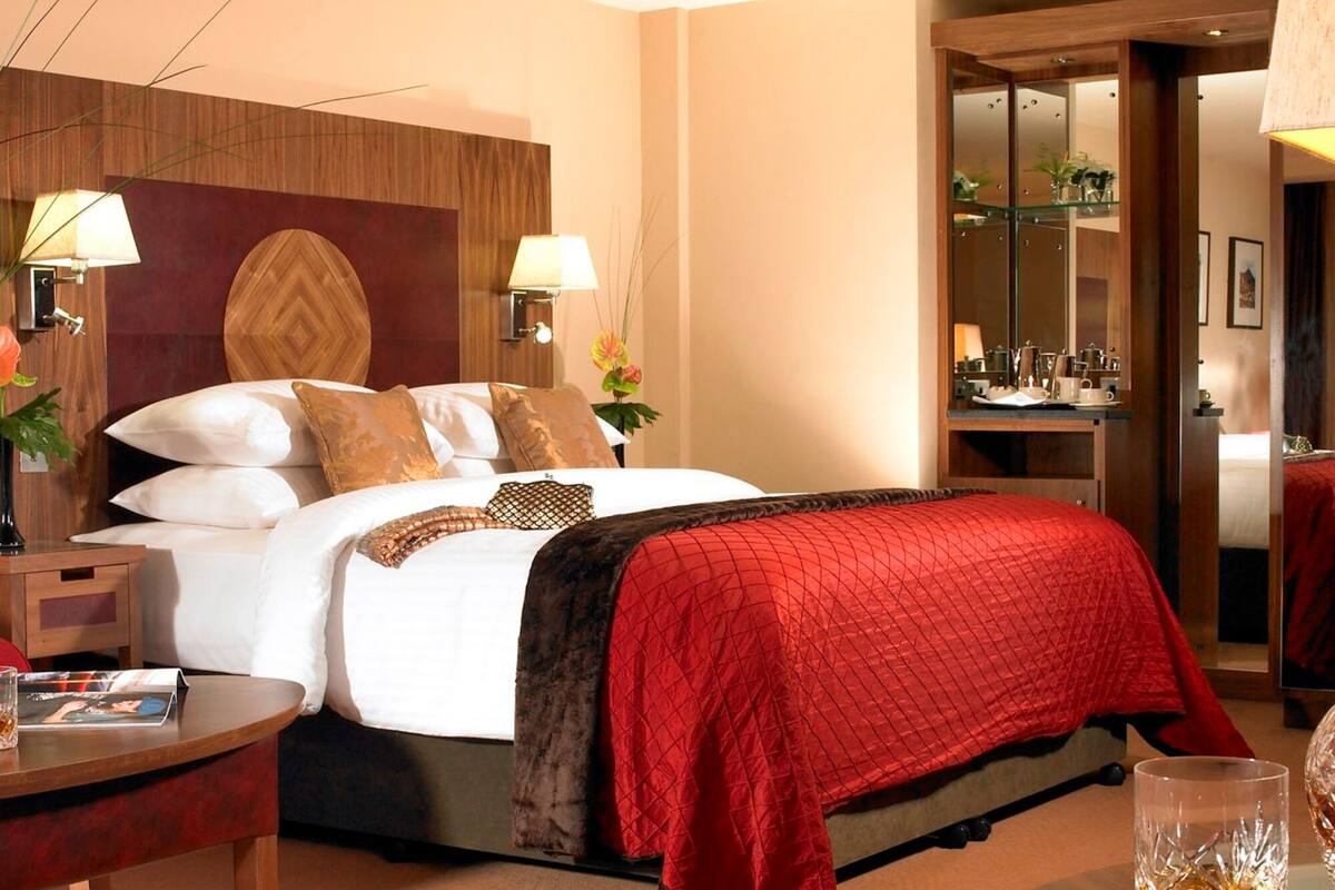 Ein Hotelzimmer mit einem großen Bett, zwei Nachttischlampen, einem Holz-Kopfteil, einem Nachttisch, einem Schreibtisch mit Lampe und einem Spiegel.