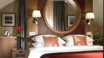 A hotel room with a large bed, two bedside lamps, a wooden headboard, a mirror, and a nightstand with a vase and a bottle.