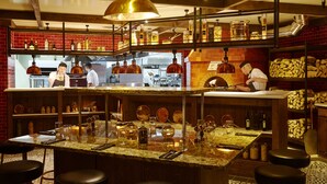 Um restaurante com um balcão central, diversas opções de assentos e cozinha visível ao fundo.