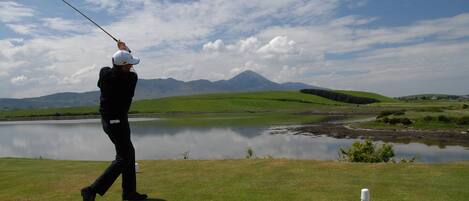 A golfer on a green with a lake and mountains in the background.