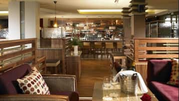 Un moderno vestíbulo de hotel con zona de bar, muebles de madera y un separador de vidrio.