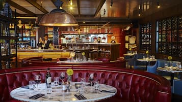 Un restaurante con cabinas de cuero rojo, mesas de mármol y una zona de bar con un cantinero.