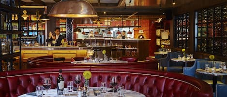 Un restaurante con cabinas de cuero rojo, mesas de mármol y una zona de bar con un cantinero.