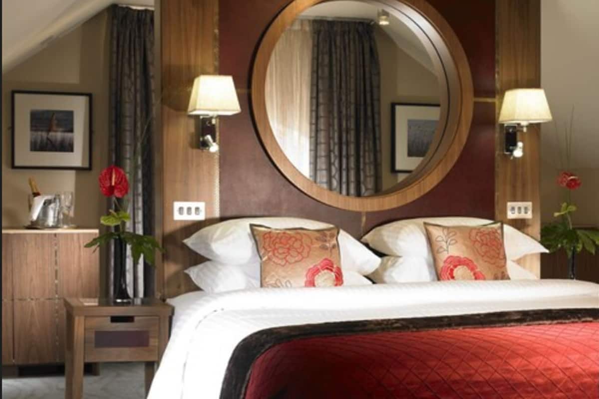 Ein Hotelzimmer mit einem großen Bett, zwei Nachttischen, einem runden Spiegel und einer roten gesteppten Bettdecke.