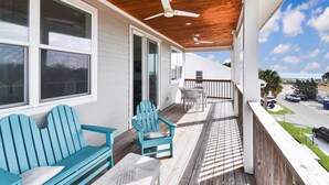 Eine überdachte Veranda mit Holzbalkendecke, einem blauen Adirondack-Sessel, einer weißen Bank und einem Tisch mit gewebtem Tischläufer.
