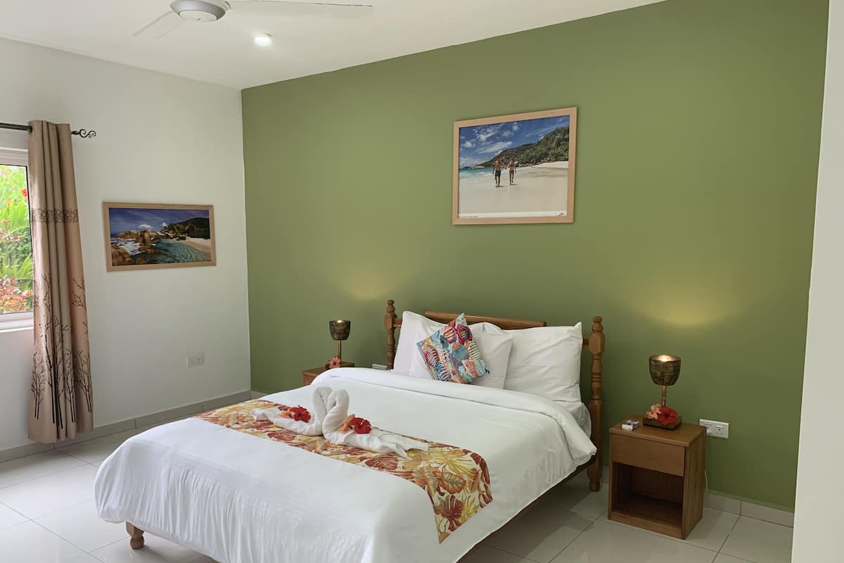 Un lit bien fait, recouvert d’une couvre-lit à motifs floraux, une photo encadrée représentant une scène de plage et une petite table de chevet avec une lampe.