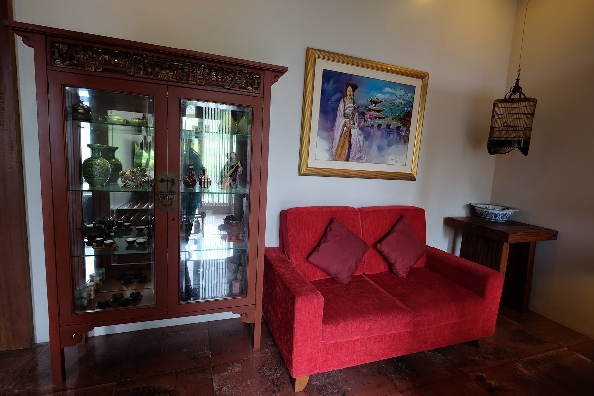 A red sofa with cushions, a glass cabinet with pottery, and a framed painting on the wall.