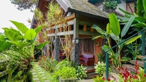 Una casa de madera tradicional con techo de paja, rodeada de exuberante vegetación tropical y un camino de piedra.