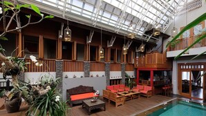 Zona de piscina interior con suelo de madera, un sofá rojo y lámparas colgantes.