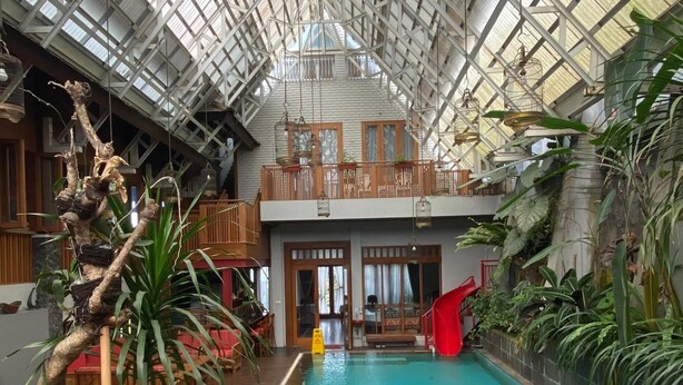 Una piscina interior con tumbonas de madera, un tobogán rojo y un techo alto con paneles de vidrio.