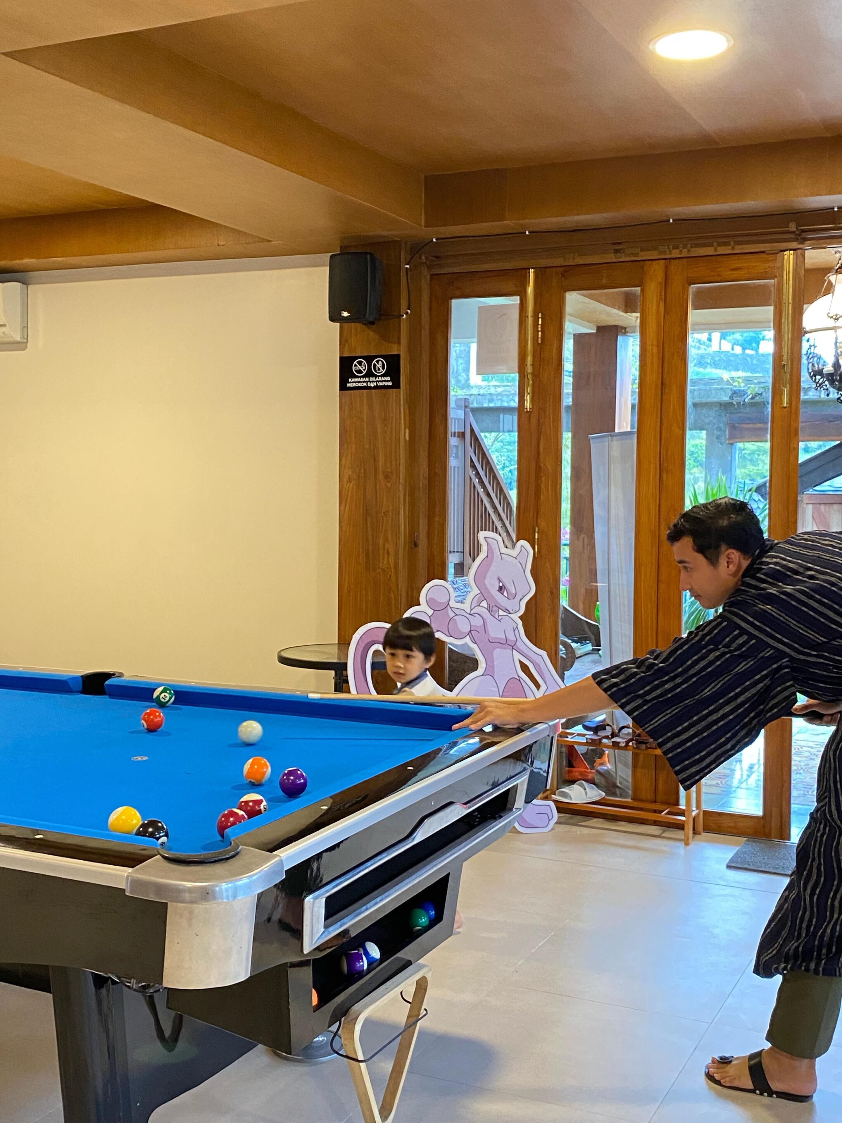 A pool table with balls, a person playing, and a child watching.