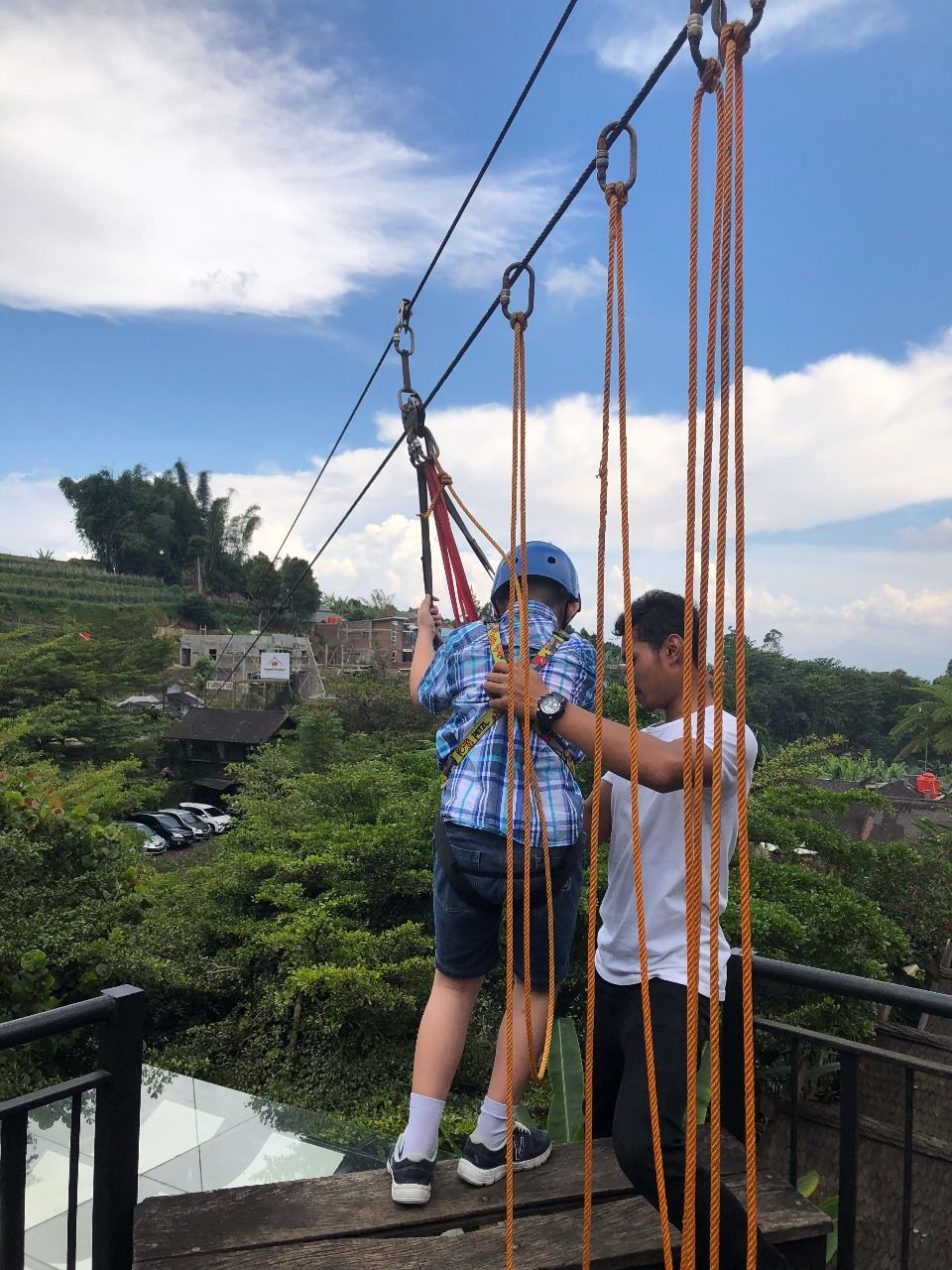 A person on a rope bridge with another person assisting.