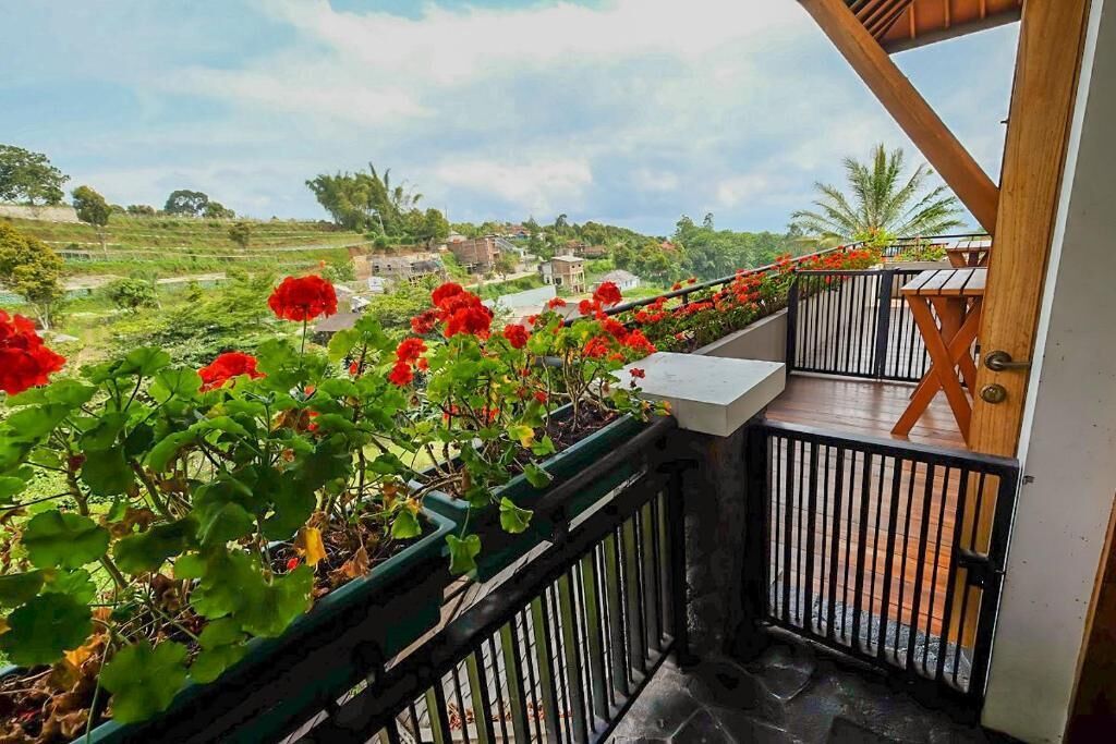 A balcony with a view of a green landscape and red flowers.